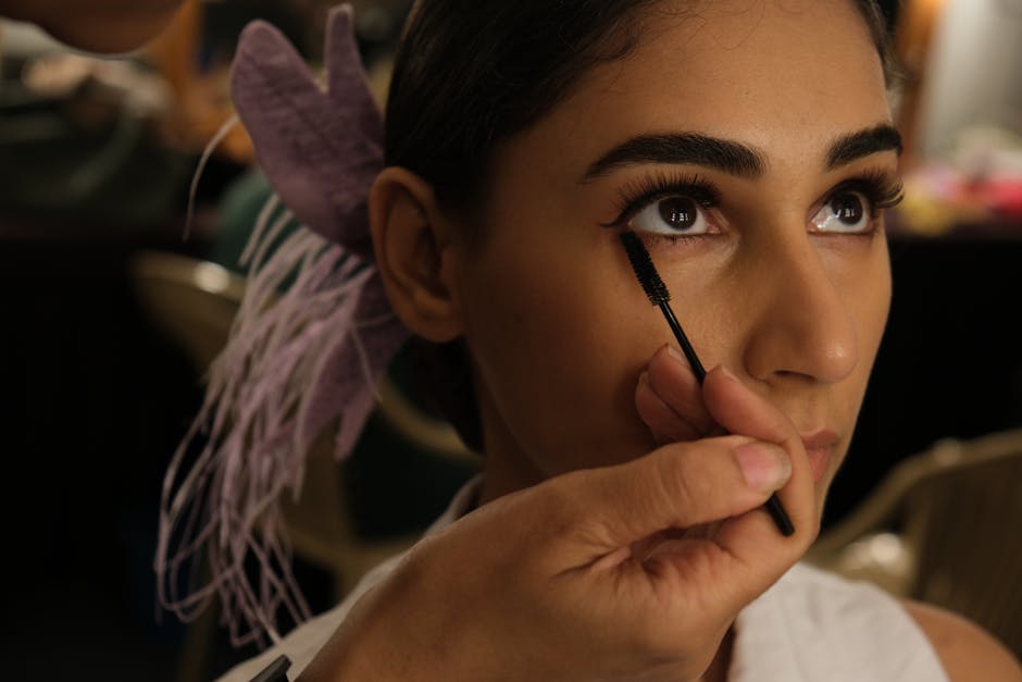 Crop visagiste applying mascara on eyelashes of gorgeous Indian woman with elegant hairstyle
