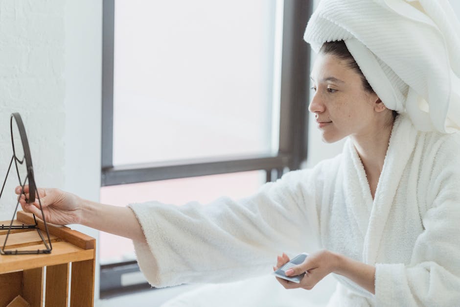 A woman in a bathrobe applying skincare in front of a mirror, emphasizing self-care.