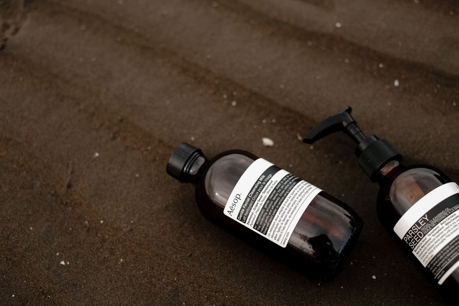 Two brown cosmetic bottles on dark sand, evoking natural skincare themes.