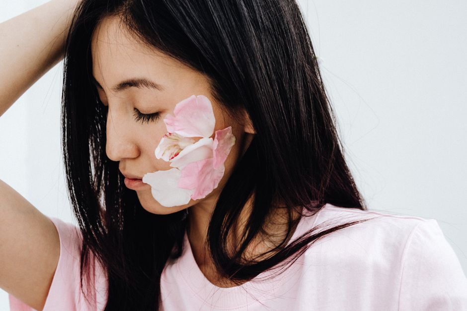 Close-up of a woman with long dark hair and pink petals on her cheek, emphasizing natural beauty.