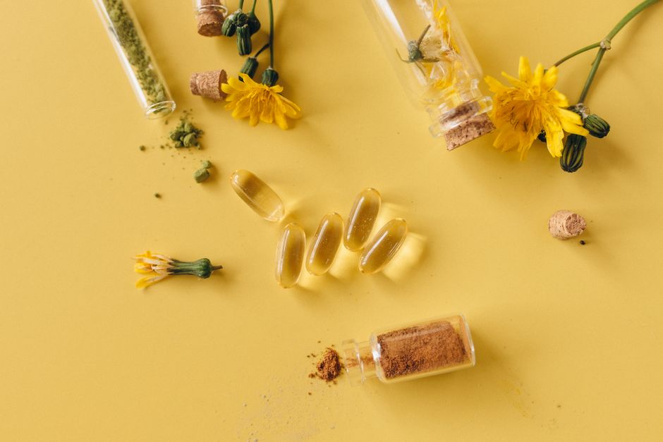 Flat lay of herbal supplements, dandelion flowers, and test tubes on a yellow background.
