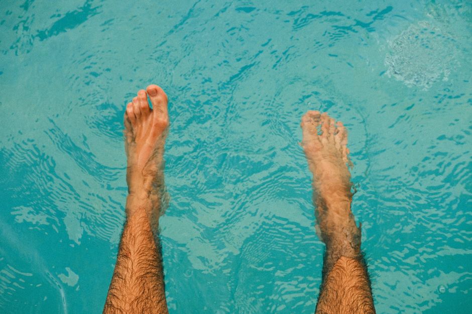 Bare feet dipped in a clear blue swimming pool, showing relaxation and leisure.