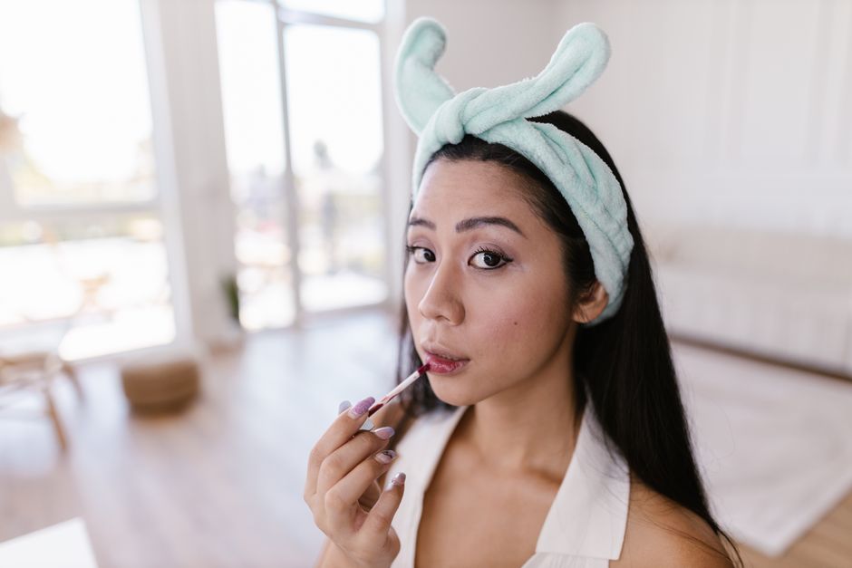 Woman with a mint headband applying lip gloss in a bright indoor setting.