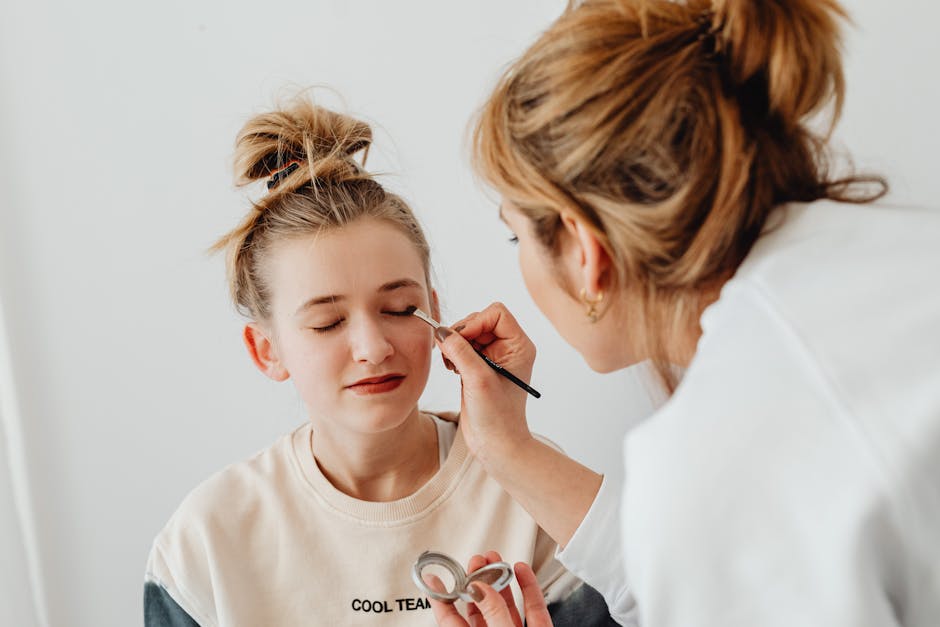A makeup artist skillfully applies eyeshadow on a teenager with a relaxed expression.