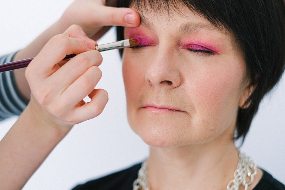 Close-up of a senior woman getting vibrant pink eye makeup applied.