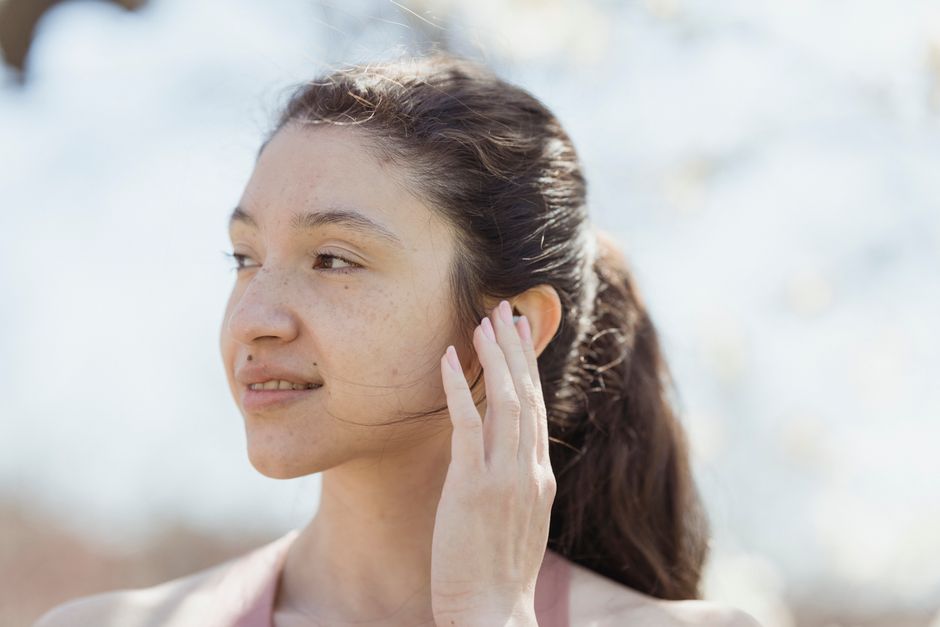 A serene outdoor portrait of a smiling brunette woman touching her ear with a natural background.