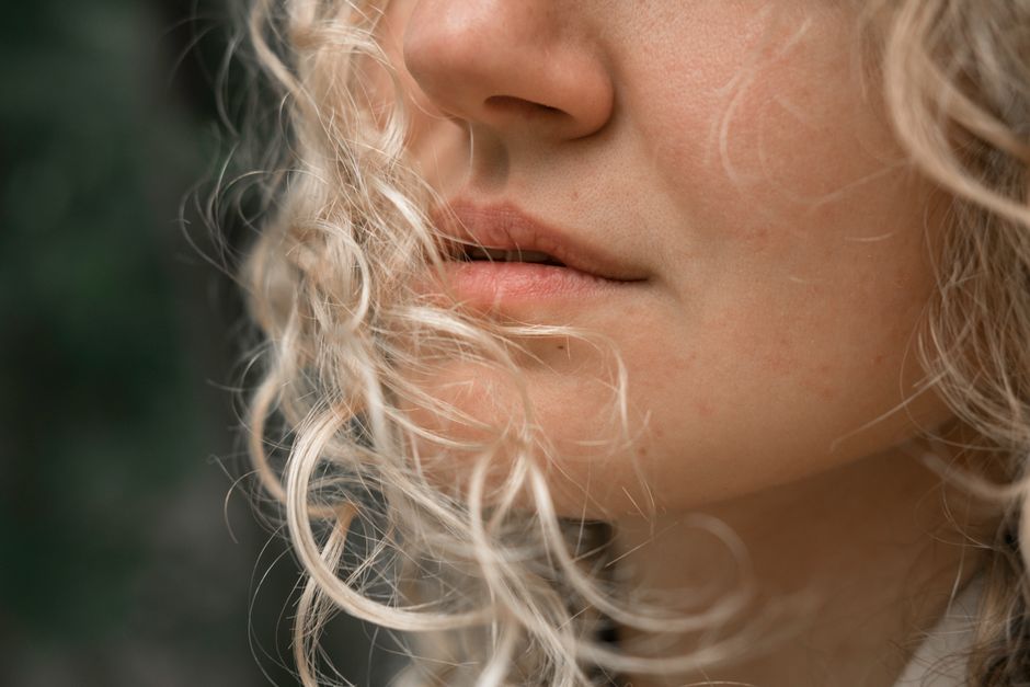 Closeup of unrecognizable female with curly blond hair and mouth opened in daylight on blurred background