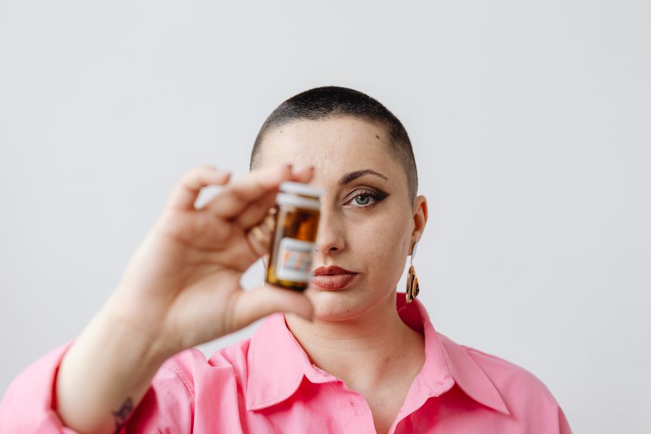 Woman in pink top holding a medicine bottle against a white background.