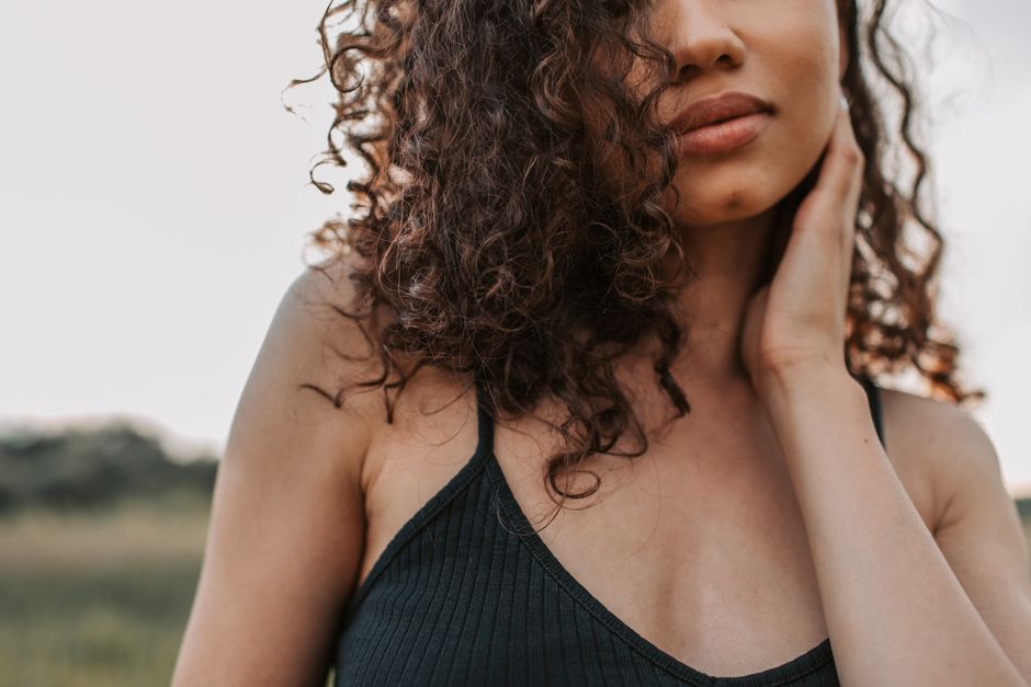 Portrait of a stylish woman with curly hair in a serene outdoor setting.