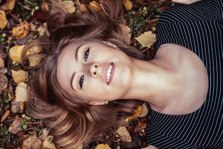 A young woman with a bright smile lies amidst vibrant autumn leaves.