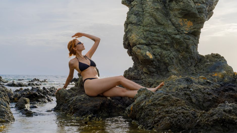 A woman in a bikini poses by rock formations on a beach in İzmir.