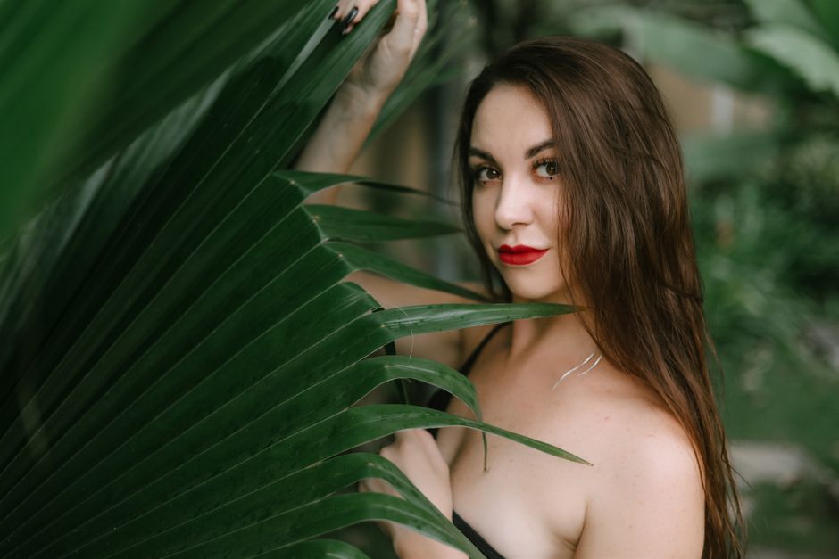 Young woman with red lips standing behind tropical leaves, creating an exotic vibe.