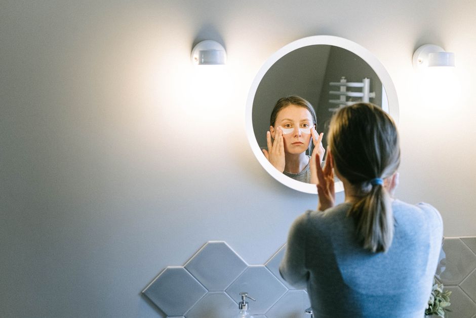 A woman applies under eye patches in a modern bathroom, emphasizing self-care.