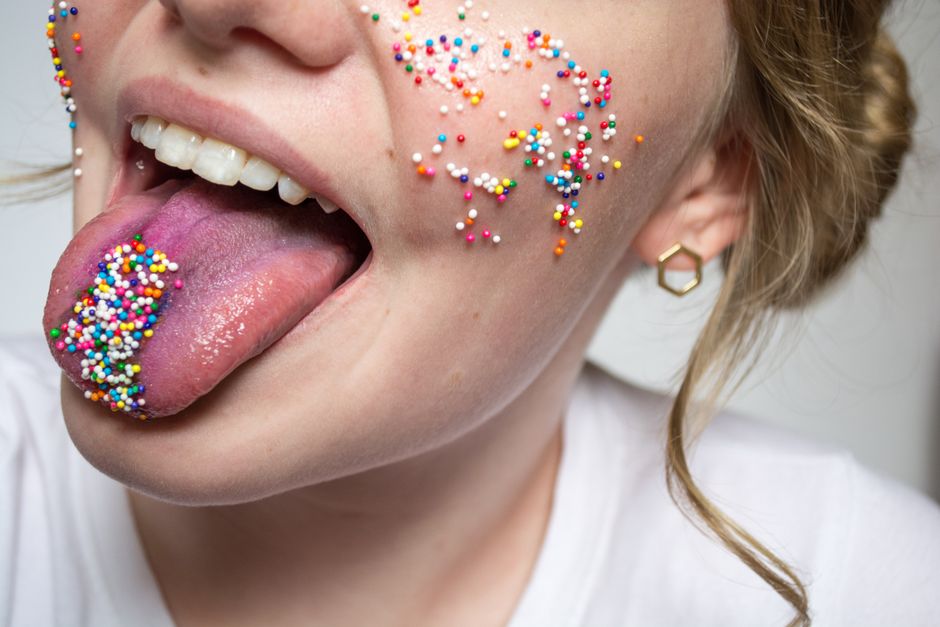 A playful close-up of a face with vibrant sprinkles on the cheek and tongue, creating a fun, colorful look.